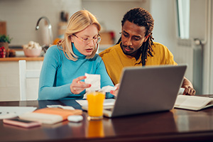 after a disaster, a couple sits at a computer going over paperwork and researching a potential fraud involving their mortgage