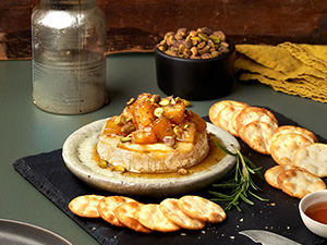 an image of some sort of holiday party dip, maybe cheese, covered in pineapple chunks and laid out on a table surrounded by crackers and a sprig of rosemary