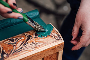 a pair of a hands holding a paint brush loaded with a bright blue color add a fresh coat to a drawer from an antique desk