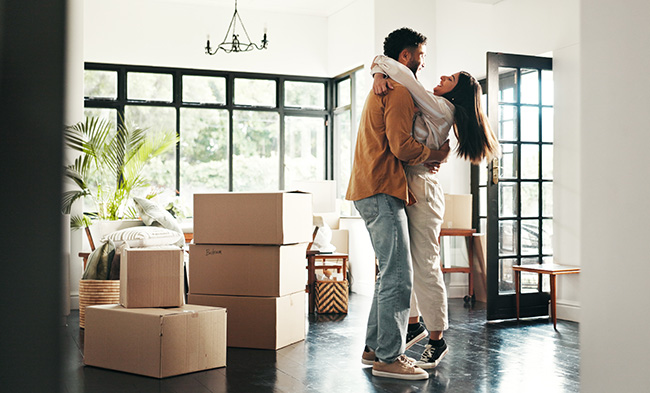 two young people surrounded by moving boxes in the living room of their new home embrace in the joy of their purchase