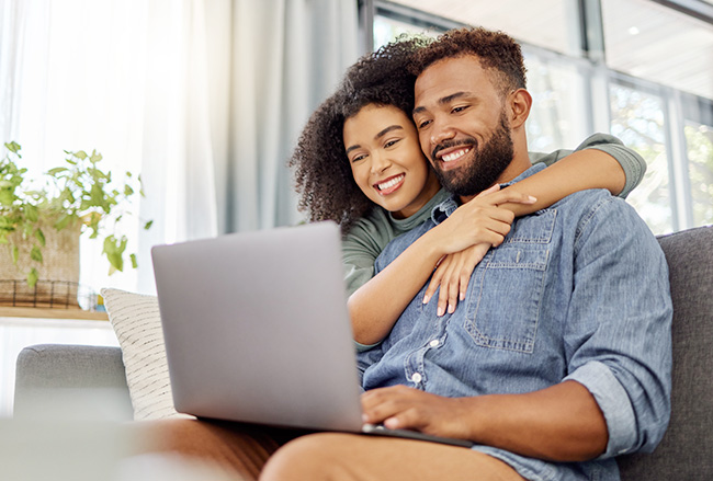 smiling couple looking at a computer together studying interest rates and mortgages before buying a house