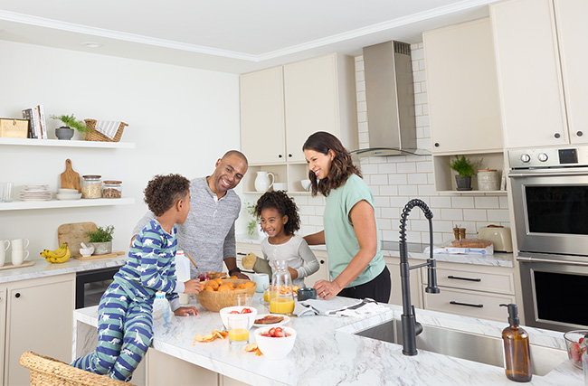 smiling family gathered in the kitchen cutting fruit and fresh squeezing orange juice, meanwhile smoke and CO detectors are working silently in the background ready to save their lives and their yellow dog in the event of a fire emergency