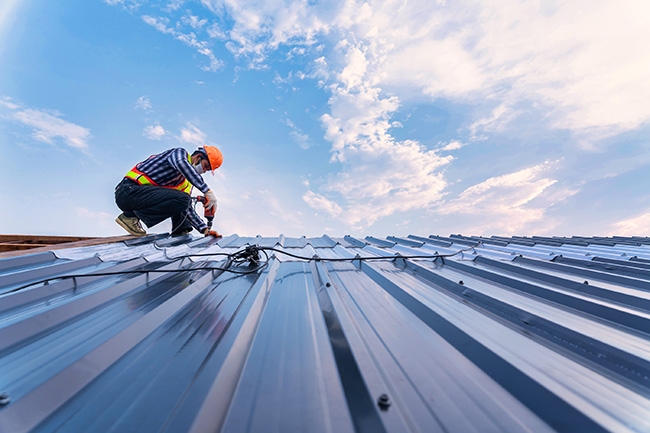 worker up on a roof installing steel roof panels on a home offering longevity, energy efficiency and safety