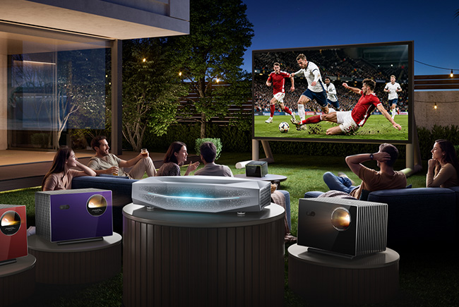 a group of friends lounge in the backyard of a posh home as a football match shows on a massive outdoor screen and the yaller dog relaxes next to the tree
